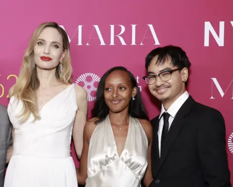 Jason Mendez/Getty Images Angelina Jolie, Zahara Marley Jolie and Maddox Chivan Jolie-Pitt, in formal attire, smile at the camera in front of a pink wall 