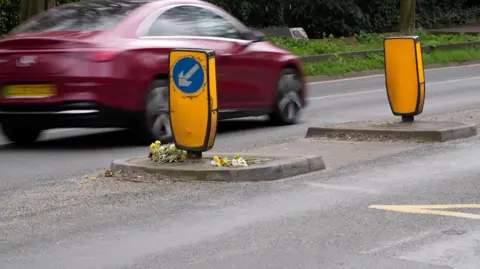 Shaun Whitmore/BBC Flowers are laid on the pavement of a central crossing of a road.