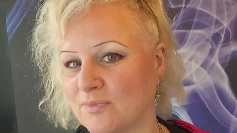 A selfie of Caroline Thorne. She has short blonde hair, pink and black eye makeup, silver earrings and a nose ring.