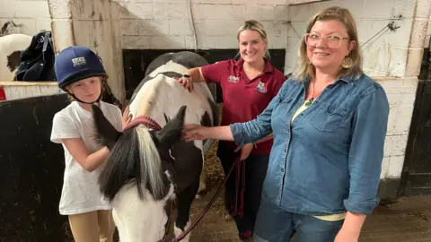 A view of Jocelyn (l) and her mother Lilias (R) along with stable manager, Cat McCartney-Kitson with a horse based at the centre.