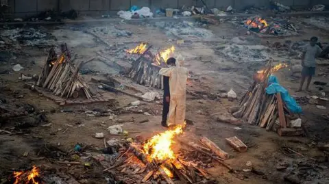 Getty Images  Family members embrace each other amid burning pyres of victims who lost their lives due to the Covid-19 coronavirus at a cremation ground in New Delhi on April 26, 2021. 