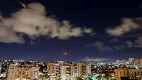 Reuters Streaks of light illuminate the sky during an attempt to intercept an Iranian missile, as seen from Ashkelon, Israel (7 April 2026)