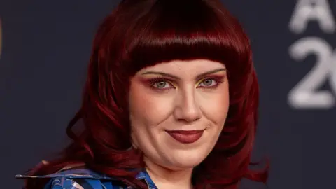 Getty Images A close-up shot of CMAT on the red carpet. Her hair is died a deep burgundy colour and styled in a bob with a straight fringe.