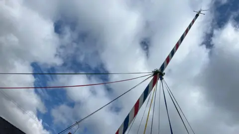 A tall maypole decorated with different coloured ribbons, taken at an angle from the ground.