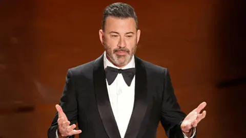 Reuters A man wearing a black suit speaks with his hands raised in front of him.