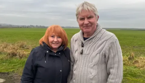 Crispin Rolfe/BBC Deborah and Shaun Coleman standing in a field. Mrs Coleman has red-coloured hair and is wearing a dark-coloured winter coat. Mr Coleman has grey hair and is wearing a beige jumper.