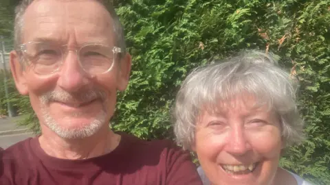 Linda Amoss A man and a woman close up shot of them smiling with some trees behind them.