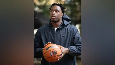 GLA OG Anunoby holding an orange basketball. He wears a black zip-up jacket.