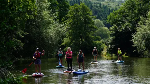 Ben Birchall/PA A group of people paddleboarding down a river