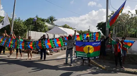 People demonstrate as French President Emmanuel Macron's motorcade drives past in Noumea, France's Pacific territory of New Caledonia, on 23 May 2024.