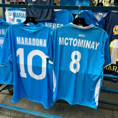 McTominay shirt hanging next to a Maradona shirt outside a shop in Naples