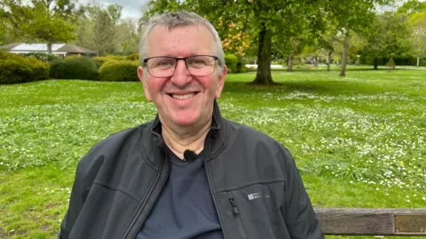 A man sits on a bench smiling.