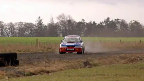 Steven Brown A rally car throwing up dust as it travels across a road in the rural Borders