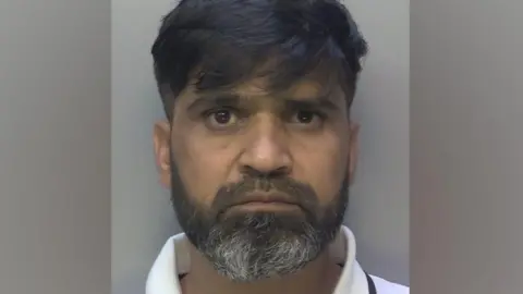 Surrey policeman shot on a man's cup. He has black and white beard and black hair with edges.