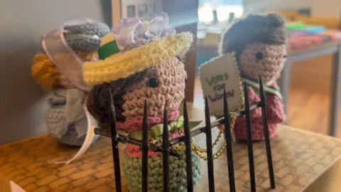 Three small knitted women - one chained to railings, another with a votes for woman placard.