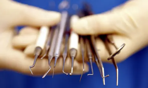 A close-up photograph of someone wearing medical gloves and holding dental equipment