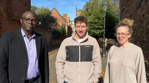 BBC Dr Abiodun Egbetokun, Brett Koenig and and Ruth McKie standing side by side on a cobbled street in the sun
