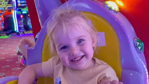 A close-up of Isabella Jonas-Wheildon sitting in an amusement ride while smiling into the camera