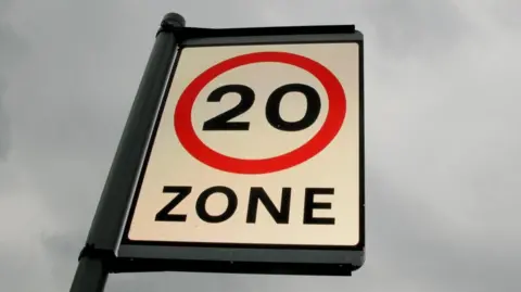 Close-up image of a 20mph zone sign, against a cloudy background.