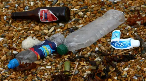 PA Media Empty glass and plastic bottles and an empty toothpaste lying on gravel.