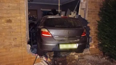Supplied A grey Vauxhall Astra that has crashed into the wall of a house leading to a living room. Bricks and debris surround the car
