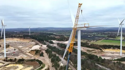 Four white wind turbines set within series of tree-lined pits 