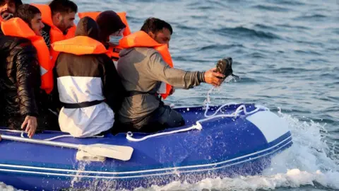 Getty Images Men in life jackets sitting in an inflatable boat . Their backs are to the camera. There is a lot of spray around the boat