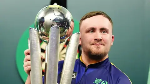 PA Media Darts world champion Luke Littler pictured holding up his trophy.