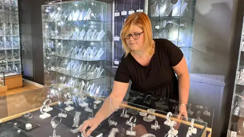 Martin Giles/BBC Woman arranging jewellery in her shop