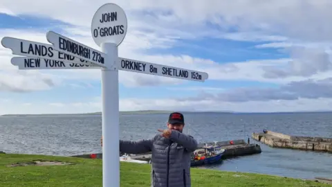 Mike Lambert A man standing at the John O'Groats sign