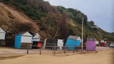 Beach huts toppled over and the sliding cliffs behind