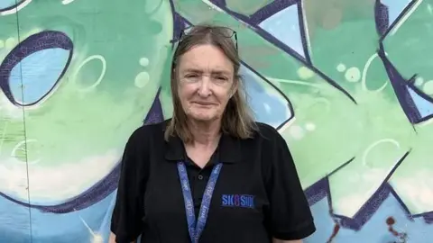 Director of Sk8side Deirdre O'Neill stands in front of a graffiti wall that says Sk8side