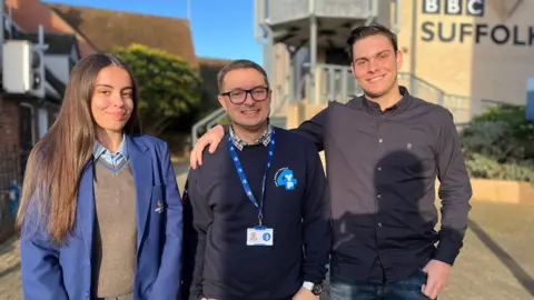 Jon Wright/BBC Kiara, a 15-year-old girl, Gavin Stone, and Reece, a 17-year-old boy, stand next to each other in front of a BBC Suffolk building 