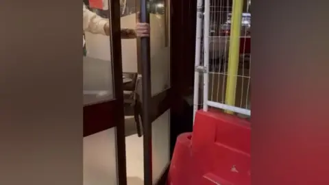 Sapore A man tries to open a fire door, which has been blocked by a red bollard.