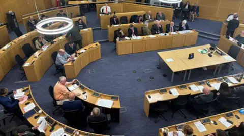 LDRS/Harry Harrison An aerial view of councillors sitting at desks in a semi circle in a modern council chamber