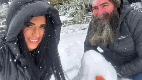 Tan Hill Inn Nicola Hayes and Paul Wright outside in the snow either side of a snowman