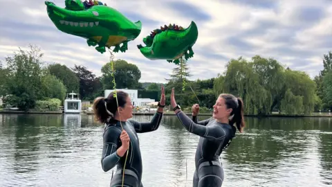 Georgia and Melissa Laurie The twins stand in front of the River Thames, wearing their wetsuits and holding the two crocodile balloons high fiving each other