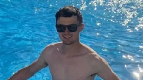 A man who is a in a swimming pool. He is wearing black sunglasses and has short dark hair. 