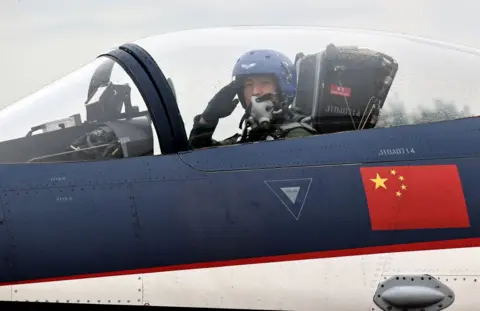 Getty Images A pilot sitting on a grounded Chinese fighter jet salutes to the camera