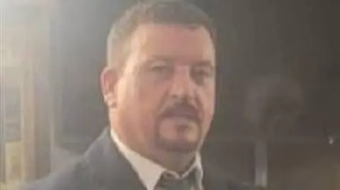 Young John Mongan is dressed in a black suit and tie and is wearing a white shirt