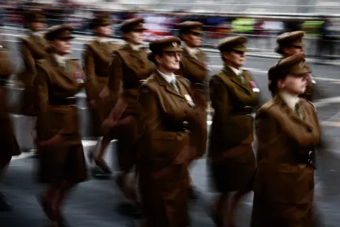 AFP Members of the military parade down the street in central London during the procession. They wear brown military uniforms with brown cadet caps with motion blur as they march.