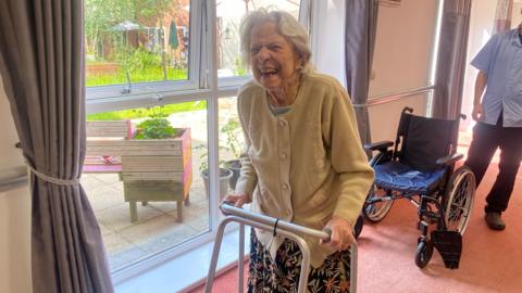 Edna Topps walks in a Zimmer frame in the corridor of her care home