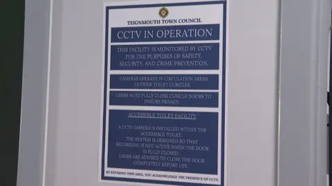 A blue sign on the wall of the Den toilets warns that CCTV is in operation and describes where in the toilets the cameras are and when the cameras are recording.