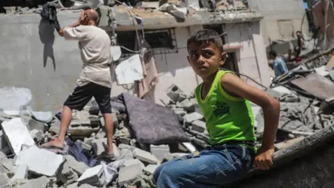 EPA A Palestinian boy sits on concrete in the Nuseirat refugee camp as a man stands in the rubble behind him