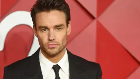 Getty Images Liam Payne, wearing a black tuxedo, poses against a red background