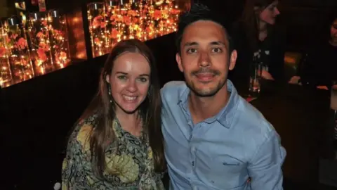 Richard Pugh and Hannah Norman smiling at the camera, dressed to go out. Richard has short dar hair and a goatee, while Hannah has long straight hair.