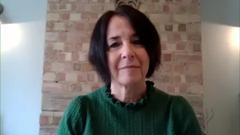 Andrea Brady, who has short dark brown hair, wears a green cable knit jumper and speaks to BBC Breakfast over a Zoom link from her home