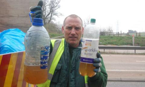 Man holding up litter in the form of plastic bottles containing liquid