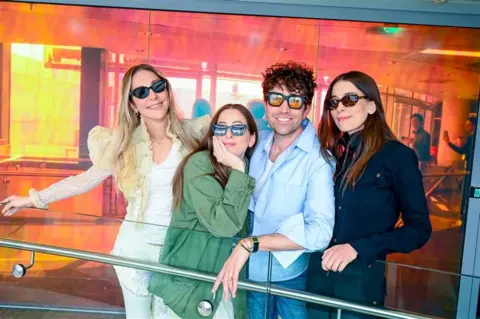 The Haim sisters with DJ Nick Grimshaw, all wearing sunglasses, in the BBC studios.