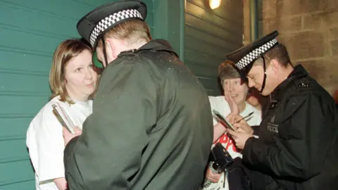 PA Media Two of the protesting women stand while two uniformed police officers speak to them and write in their notebooks.
